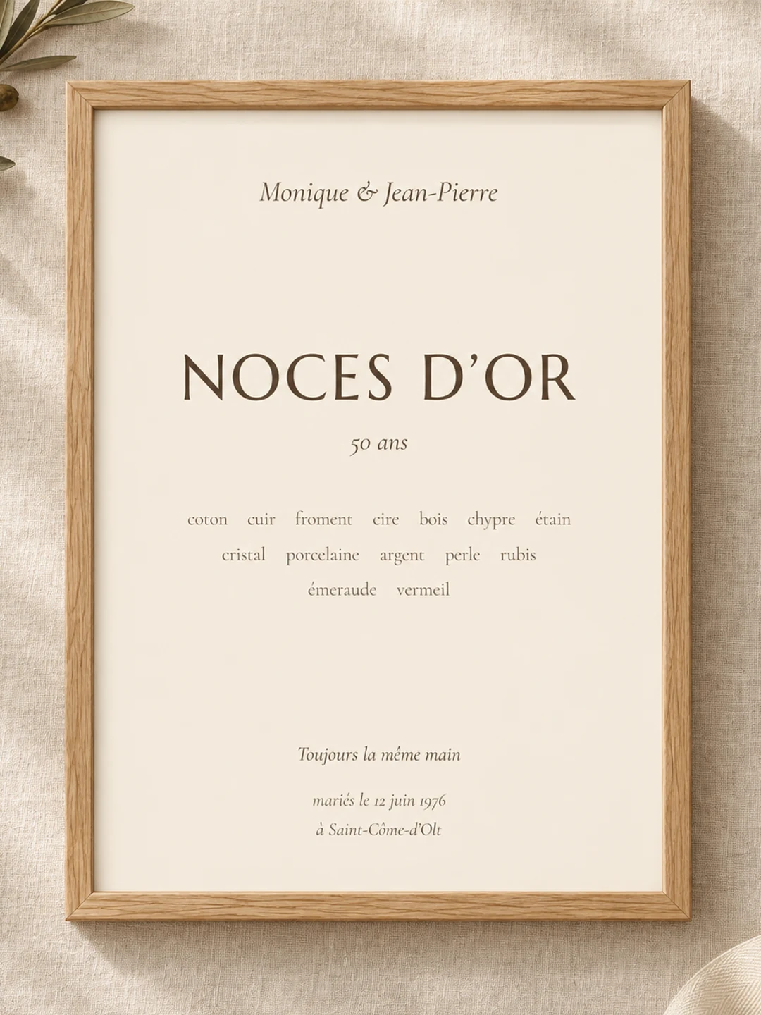 Affiche Noces d’or dans son cadre en bois clair, posée à plat sur du lin avec un rameau d’olivier