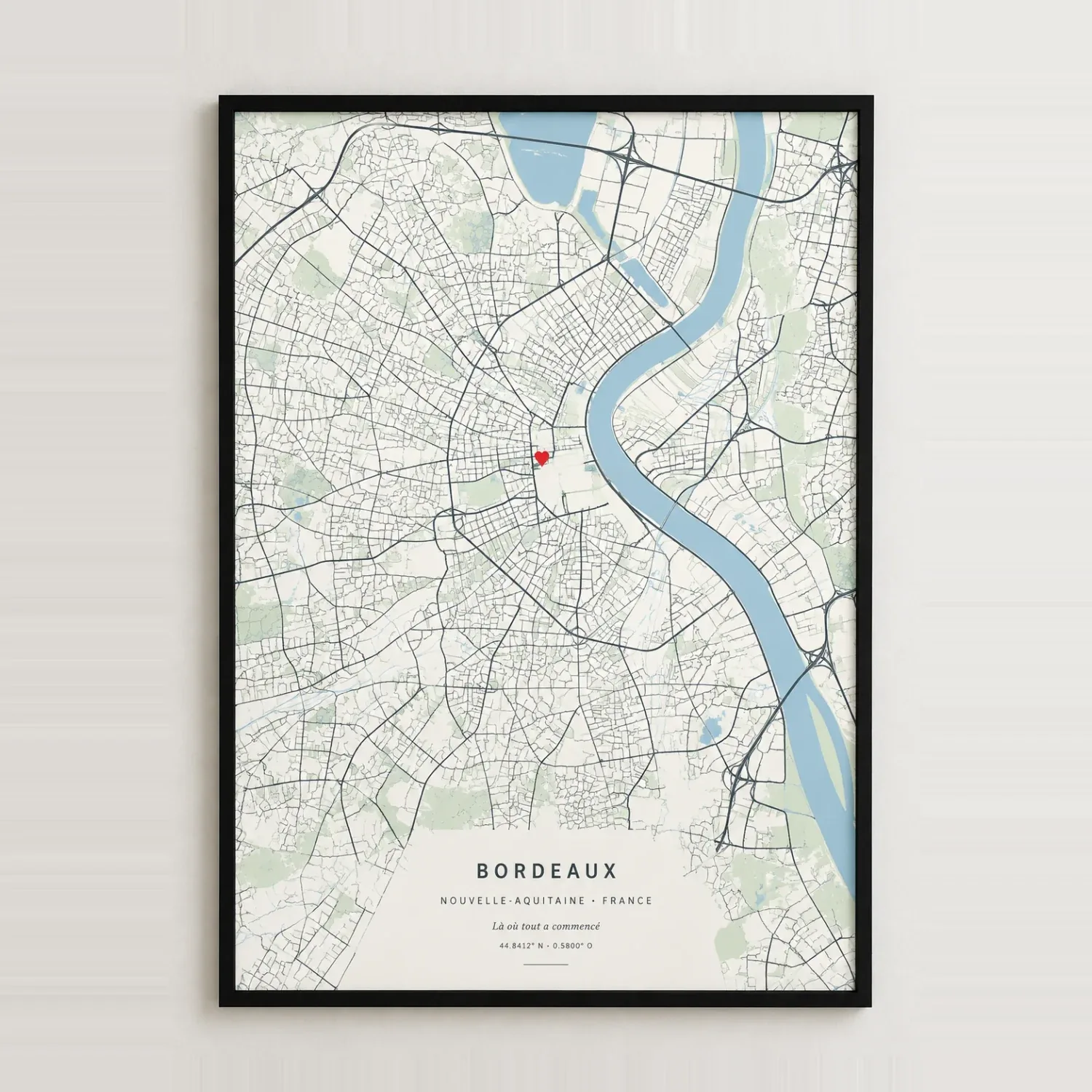 Map poster of Bordeaux, blue Garonne and a red heart on cream, in a black frame on a pale wall, shown in the French version