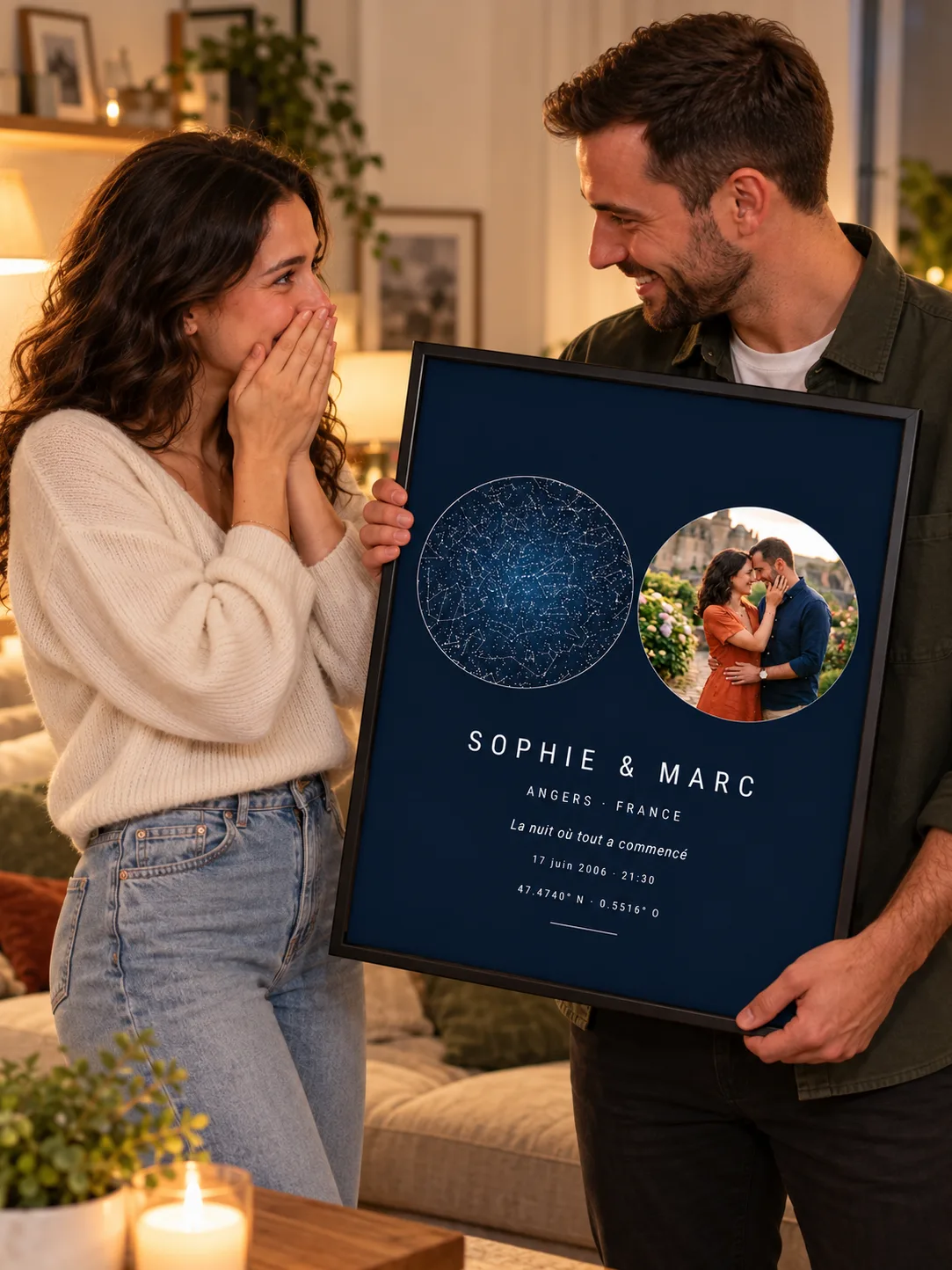 Un homme tient une affiche bleu nuit dans un cadre noir, ciel étoilé et photo ronde du couple côte à côte, « Sophie & Marc » ; la femme à côté de lui, les mains sur la bouche, rit d’émotion