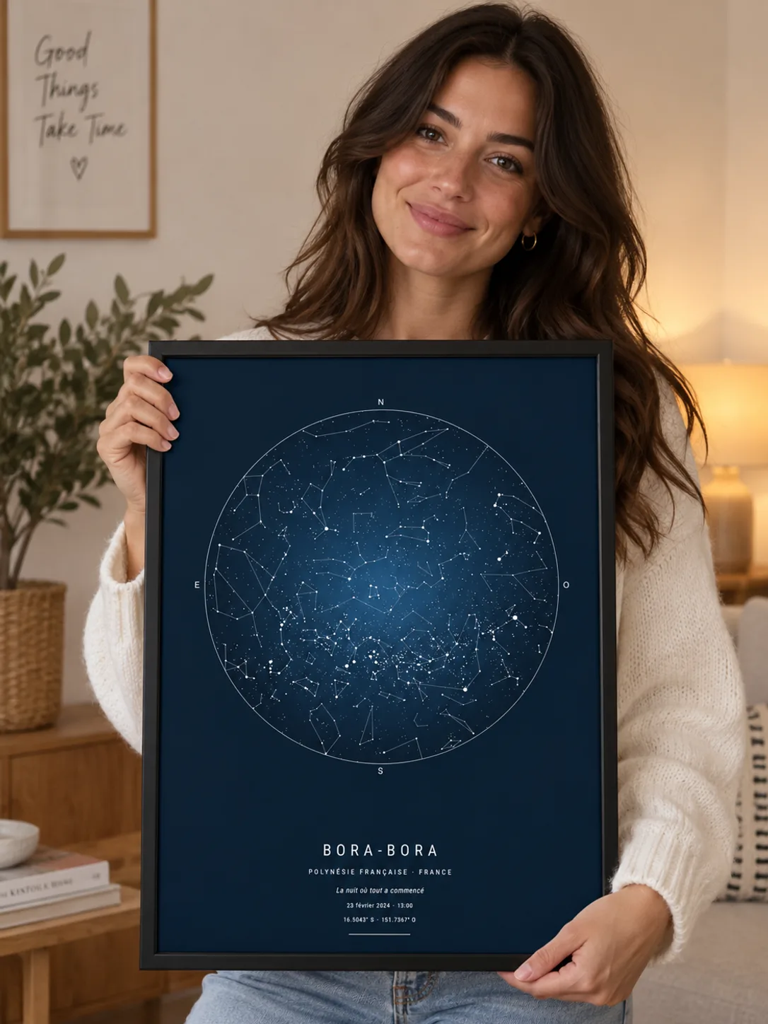 Une femme tient une affiche carte du ciel de Bora-Bora encadrée de noir, dans un salon