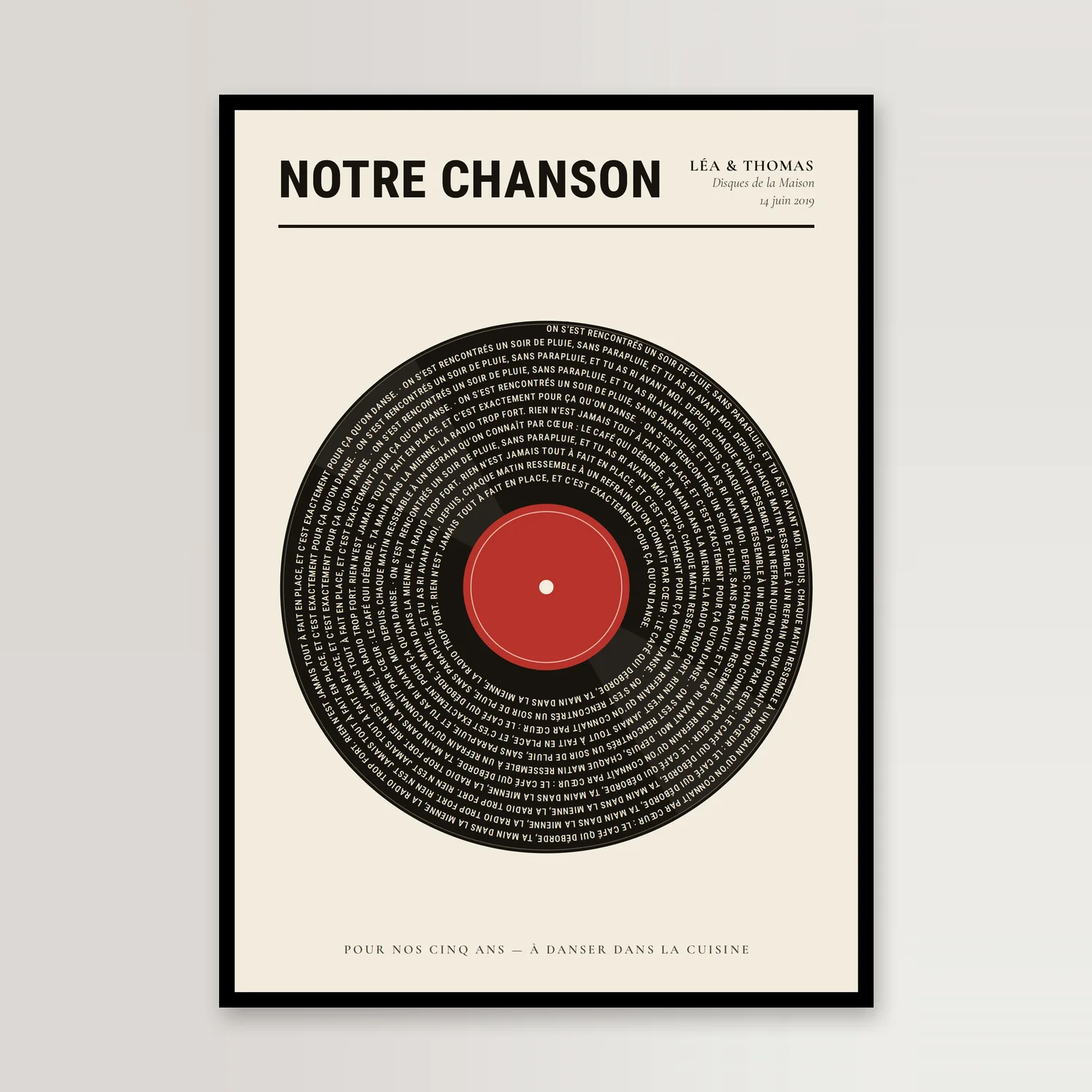 Affiche disque vinyle dans un cadre noir : un disque noir aux sillons de texte ivoire et à l’étiquette rouge, titre « Notre chanson » en capitales, contre un mur clair