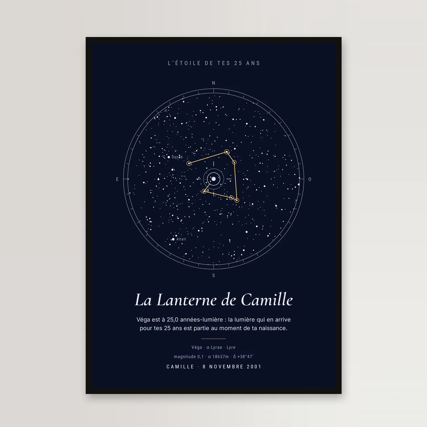 Affiche bleu nuit dans un cadre noir, sur un mur clair : un ciel étoilé rond centré sur Véga, une constellation dorée tracée autour, « La Lanterne de Camille » en italique et « L’étoile de tes 25 ans » en haut