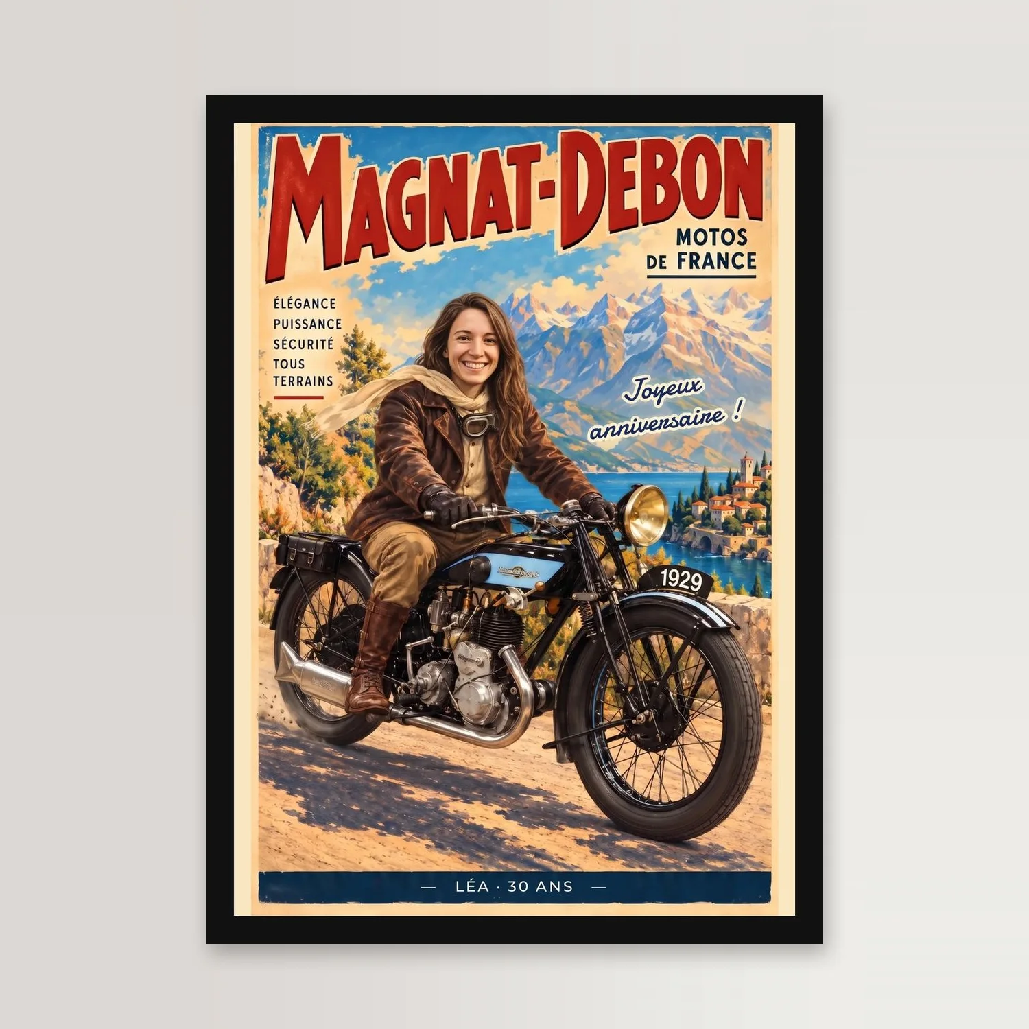 Affiche de moto vintage dans un cadre noir sur un mur clair : titre MAGNAT-DEBON en capitales rouges, une motarde aux longs cheveux châtains, veste de cuir brun et écharpe crème, sur une moto de 1929 noire et bleu ciel devant des montagnes et un lac, phrase « Joyeux anniversaire ! » et bandeau bleu « LÉA · 30 ANS »