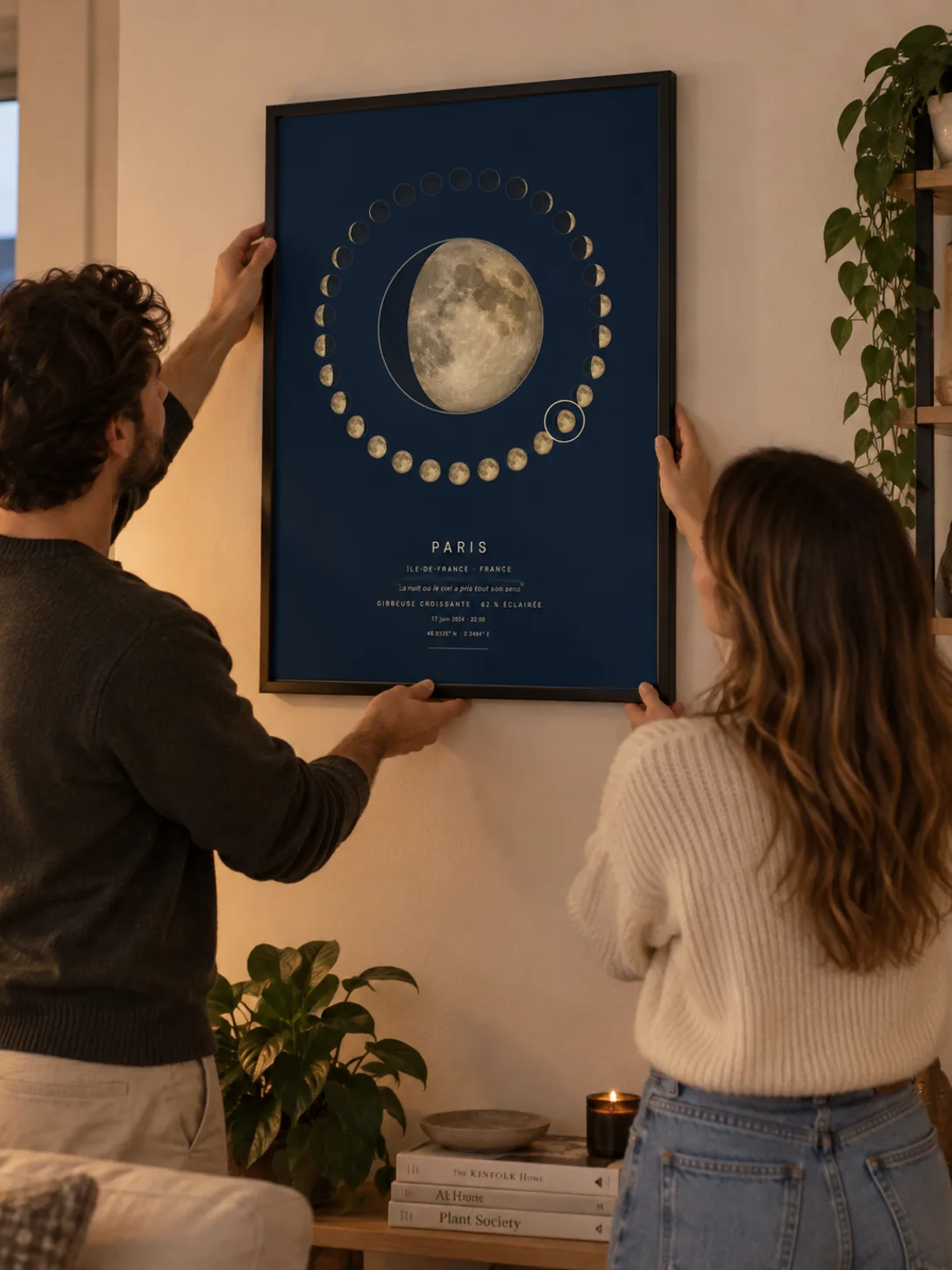 Un couple accroche au mur d’un salon une affiche phase de lune encadrée de noir