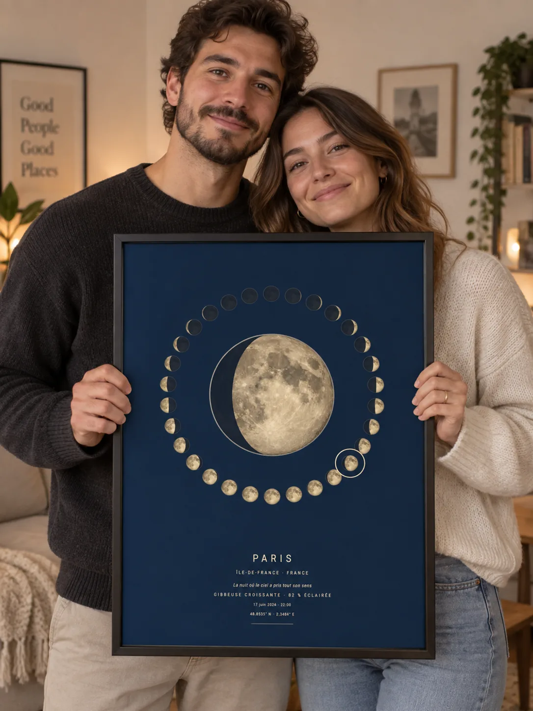 Un couple tient une affiche phase de lune de Paris encadrée de noir, dans un salon