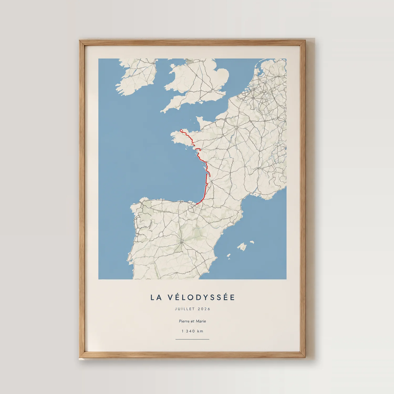 Affiche trajet personnalisée de La Vélodyssée, tracé rouge sur carte, dans un cadre en bois clair contre un mur