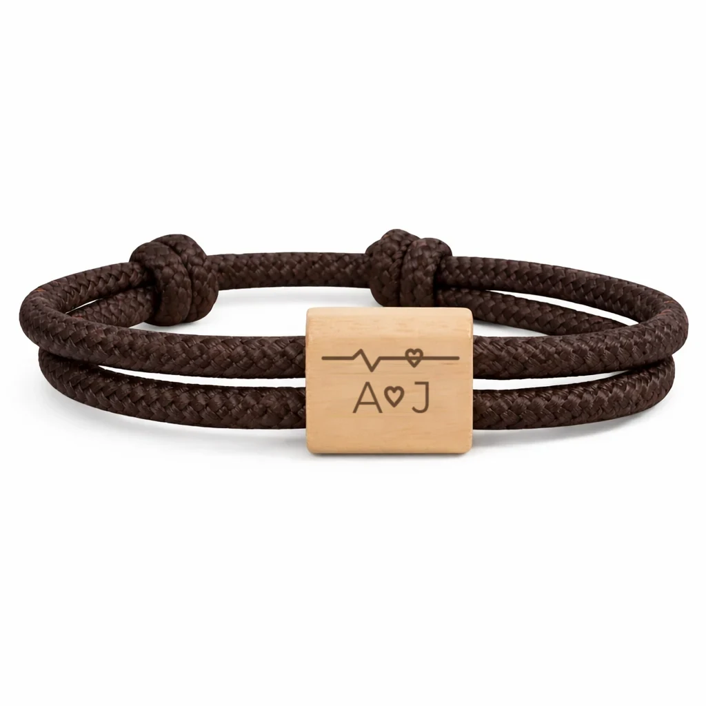 Photographie du bracelet Battement de cœur, cordon marron : cordon marin double à nœuds coulissants et une plaque en bois de cerisier, gravée d’un tracé de battement de cœur et de deux initiales.