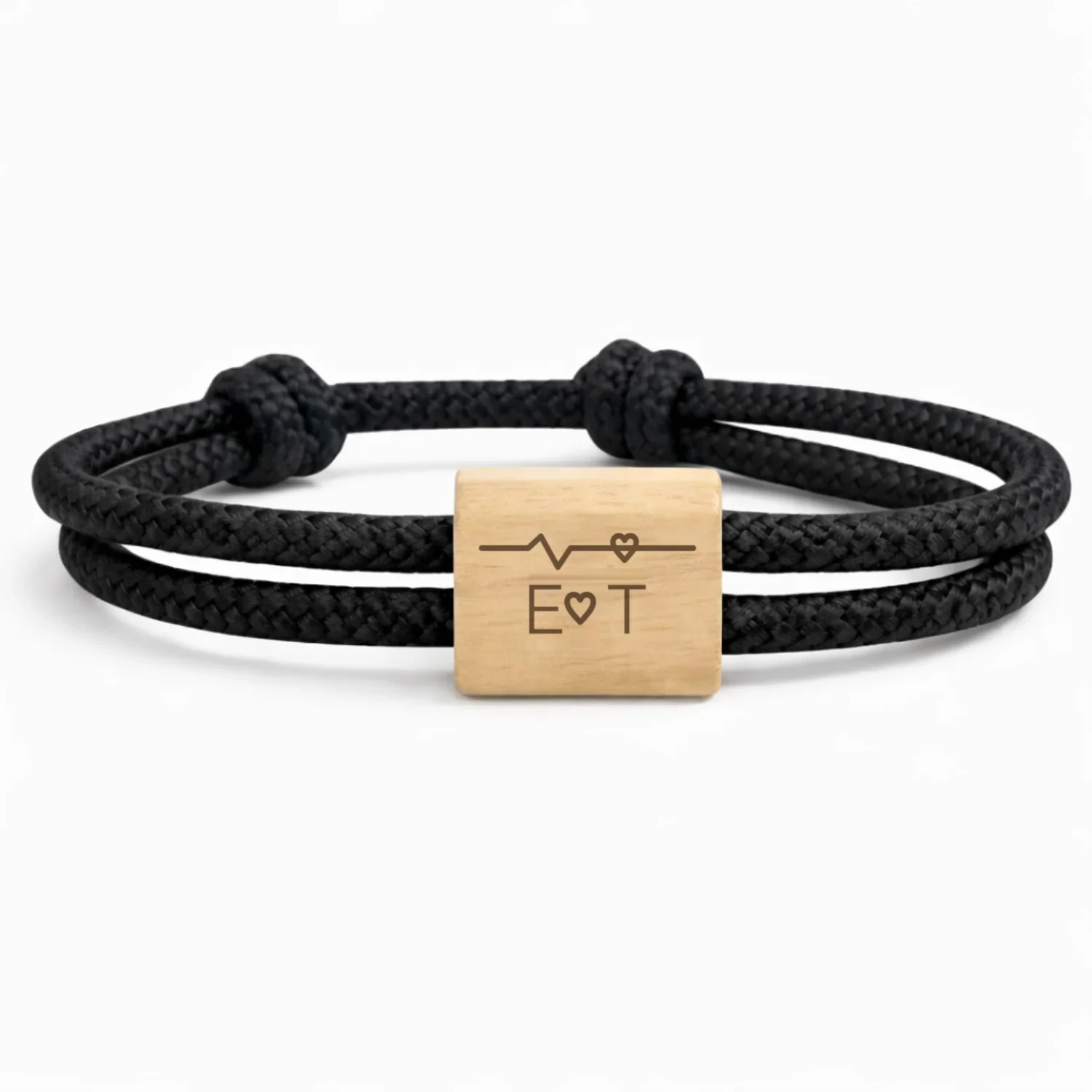 Photographie du bracelet Battement de cœur, cordon noir : cordon marin double à nœuds coulissants et une plaque en bois de cerisier, gravée d’un tracé de battement de cœur et de deux initiales.