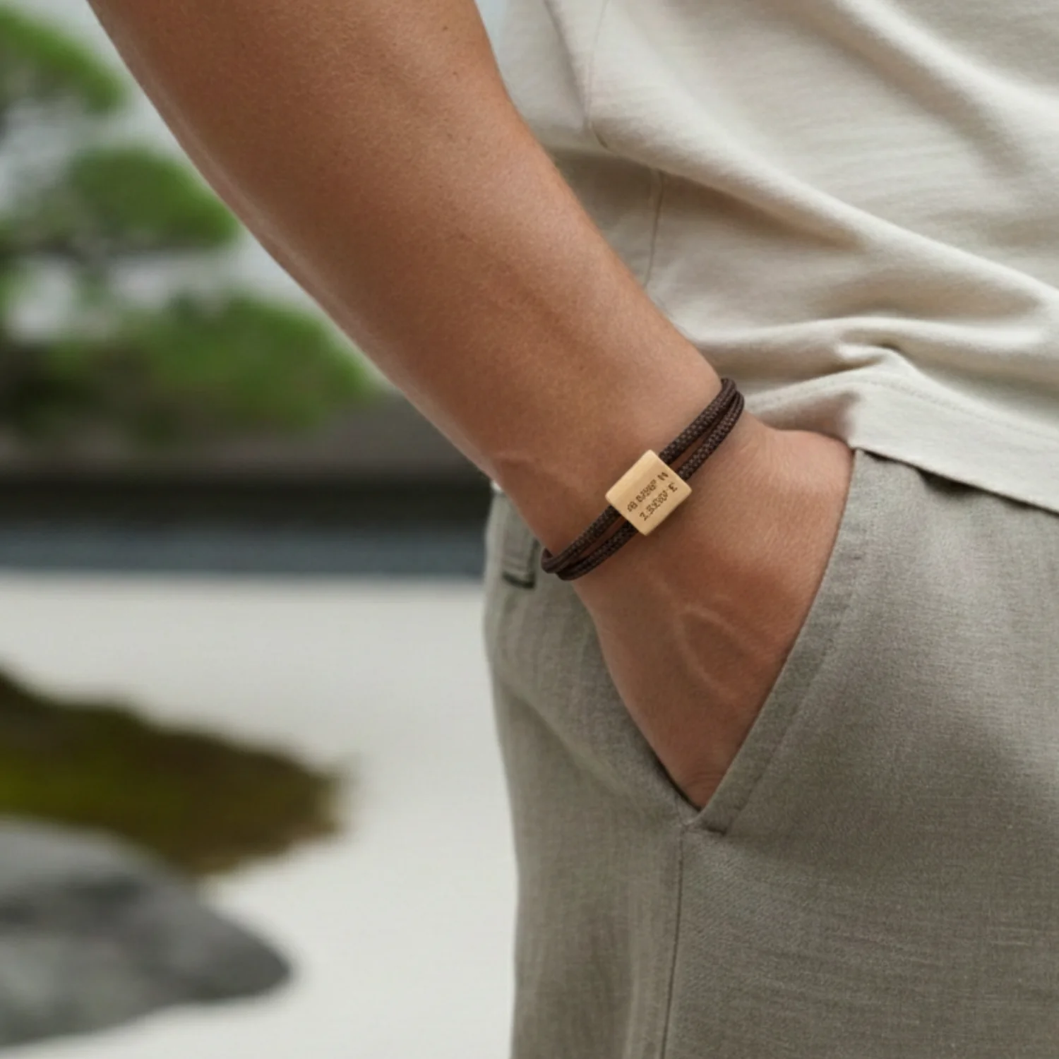 Bracelet marron porté au poignet, main dans la poche d'un pantalon de lin clair