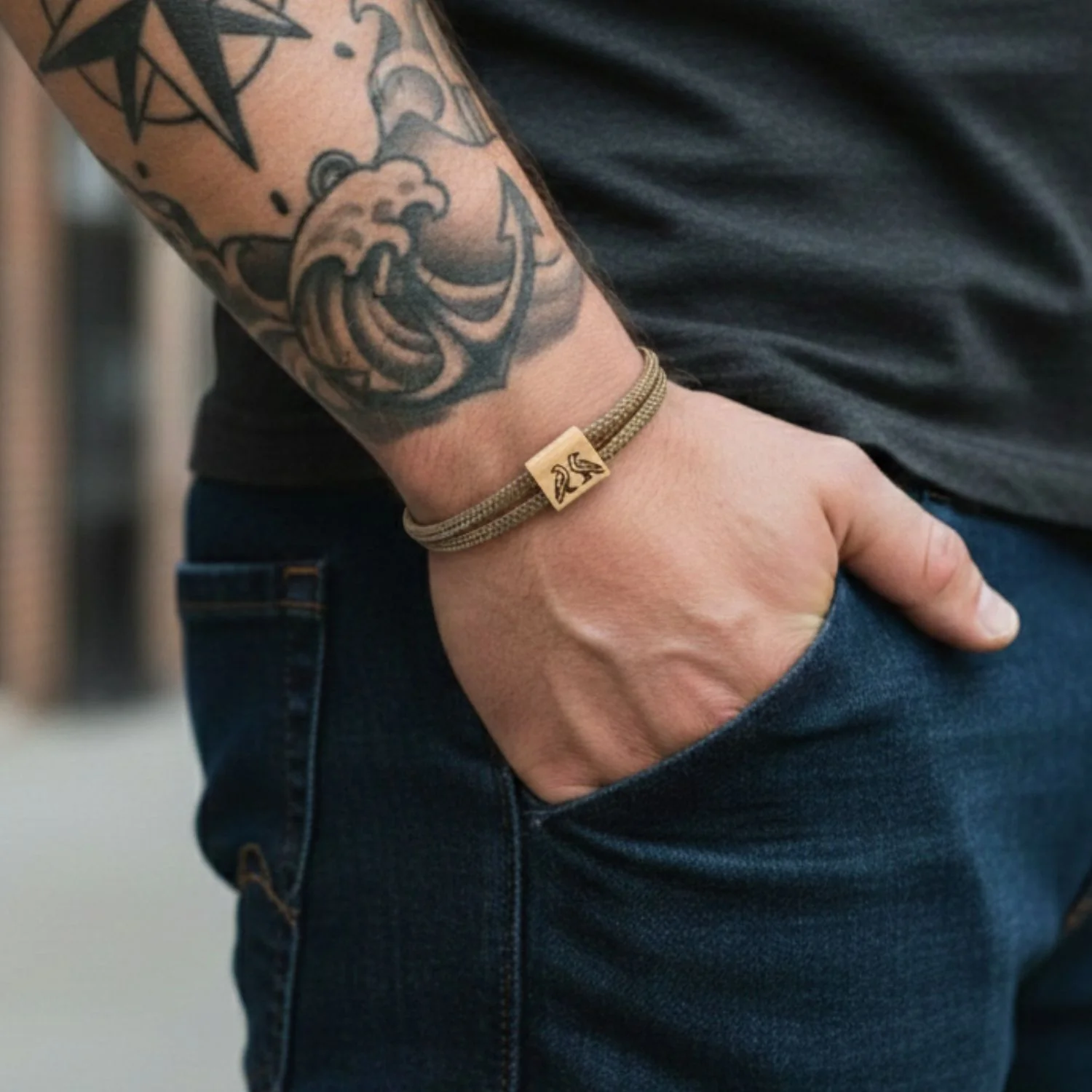 Bracelet porté au poignet d'un homme tatoué, main dans la poche d'un jean