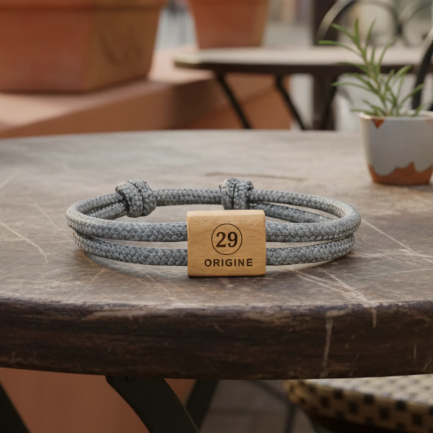 Numéro 29 gravé, cordon gris chiné, bracelet posé sur une table en pierre