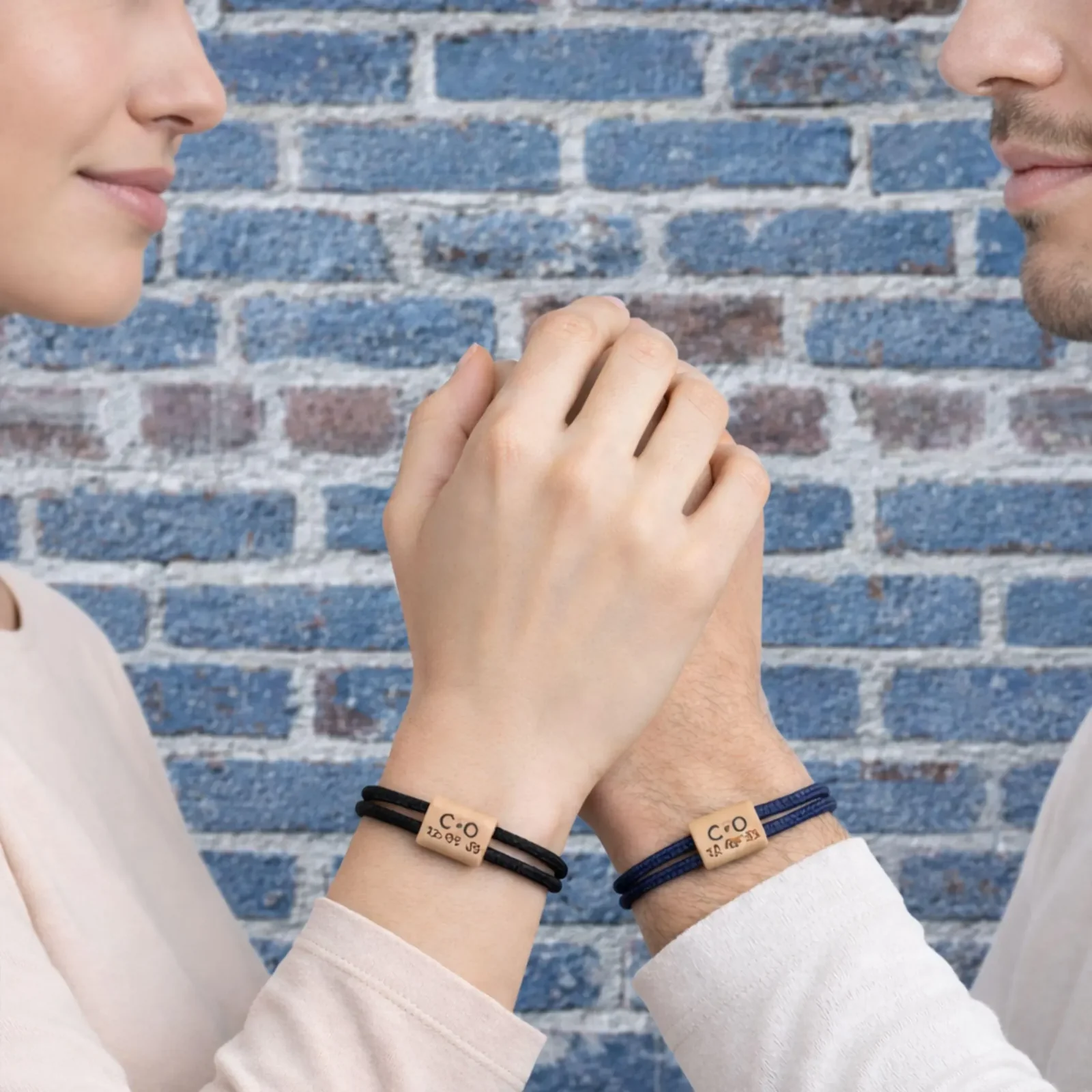 Deux bracelets portés par un couple qui se tient la main devant un mur de briques