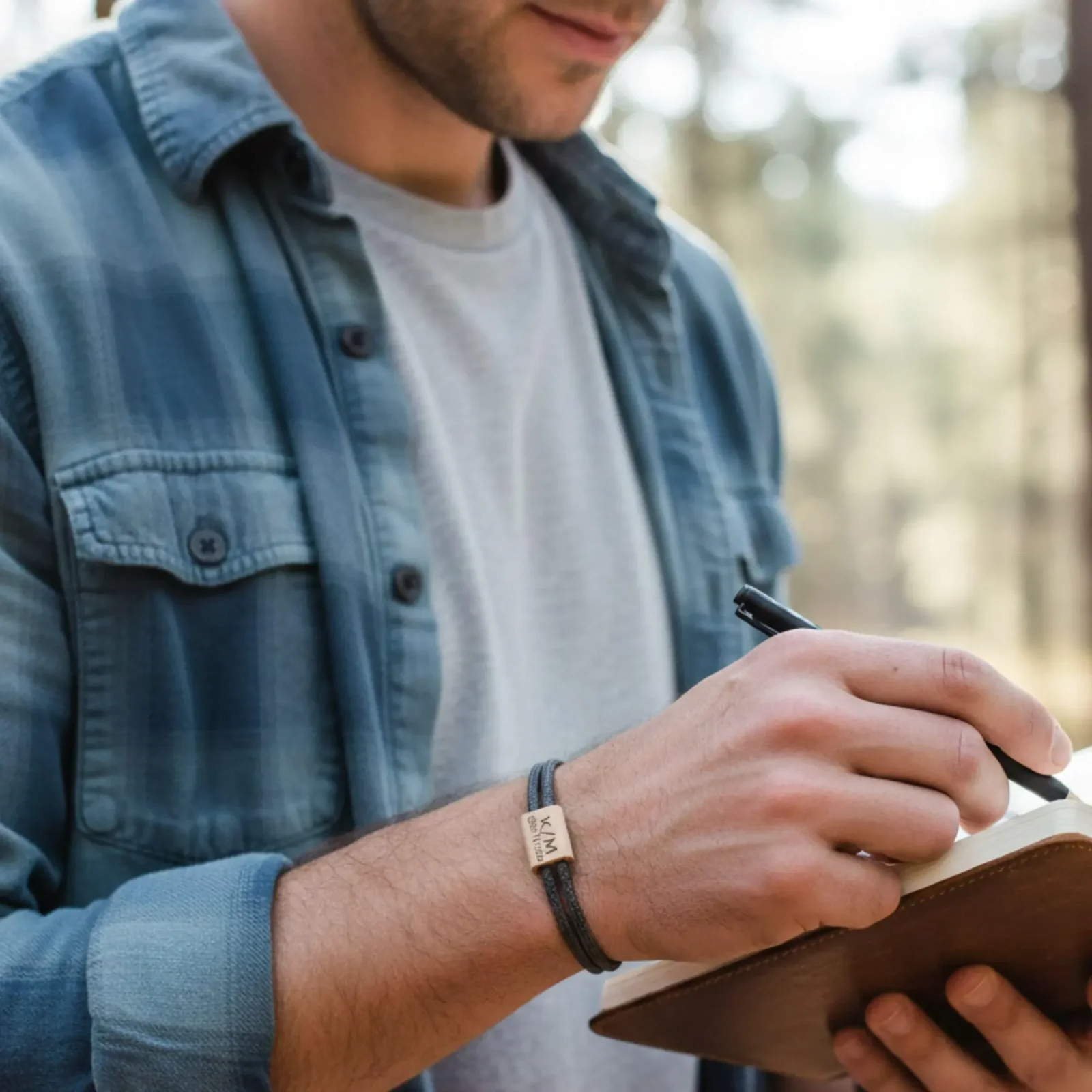 Bracelet porté au poignet d'un homme qui écrit dans un carnet, en extérieur