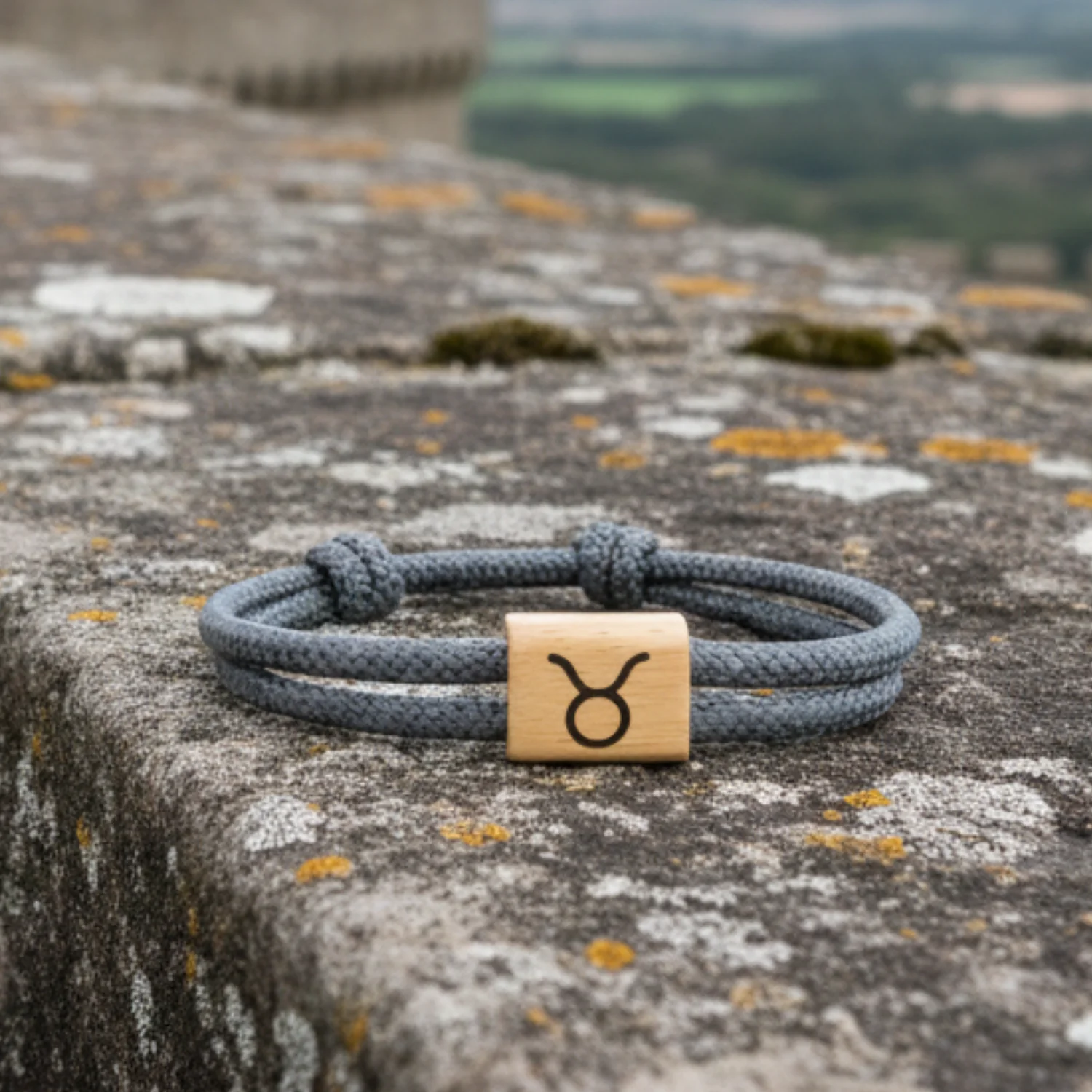 Bracelet gravé du Taureau posé sur un muret de pierre, campagne en arrière-plan