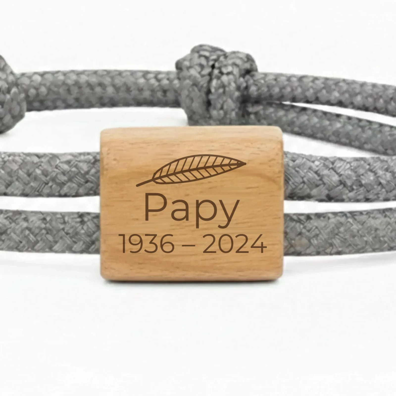 Photographie du bracelet souvenir Plume : gros plan de la pièce en bois de cerisier, gravée d’une plume, d’un prénom et de deux dates.