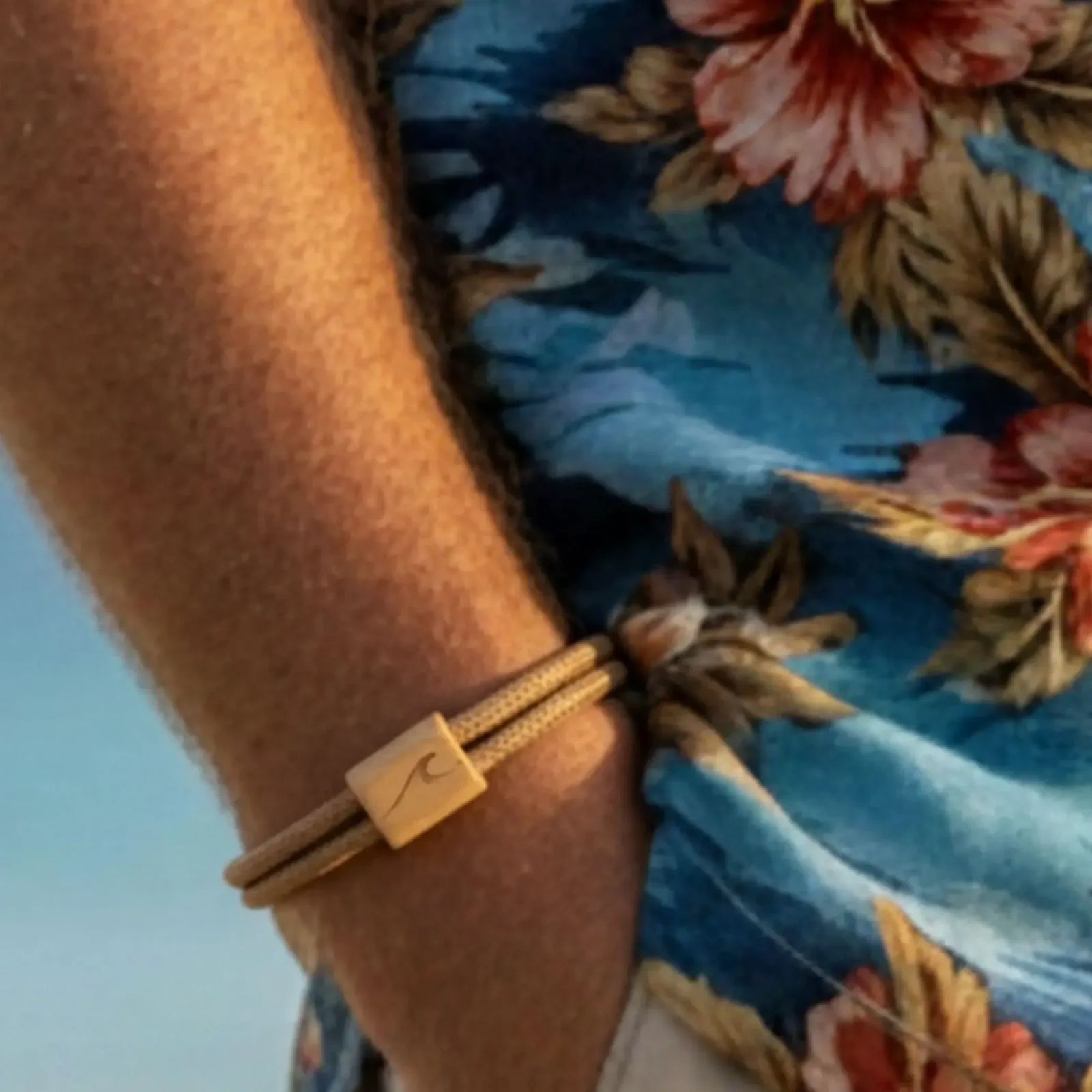 Bracelet caramel porté au poignet, devant une chemise à fleurs